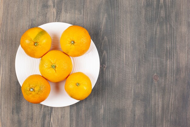 Une assiette blanche pleine de mandarines fraîches et sucrées. Photo de haute qualité