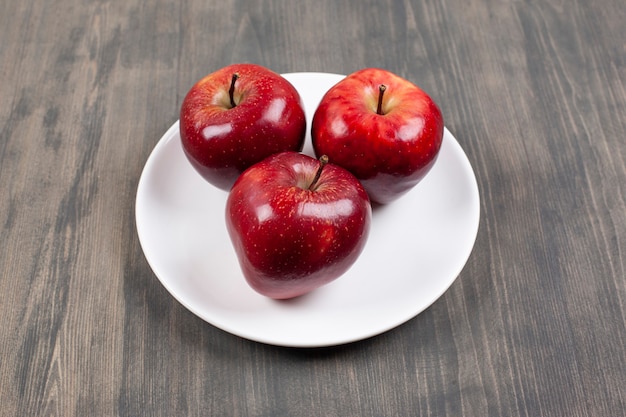 Une assiette blanche avec des pommes juteuses rouges sur une table en bois. Photo de haute qualité