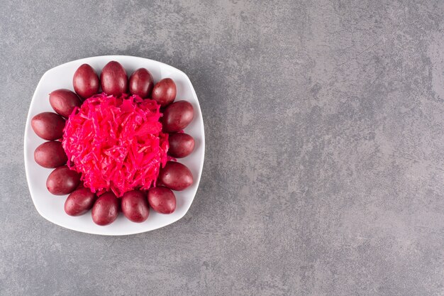 Assiette blanche de prunes marinées et de chou sur table en pierre.
