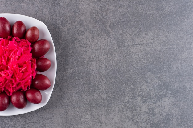 Assiette blanche de prunes marinées et de chou sur table en pierre.