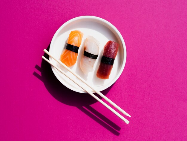 Assiette blanche de sushis avec des baguettes sur un fond rose