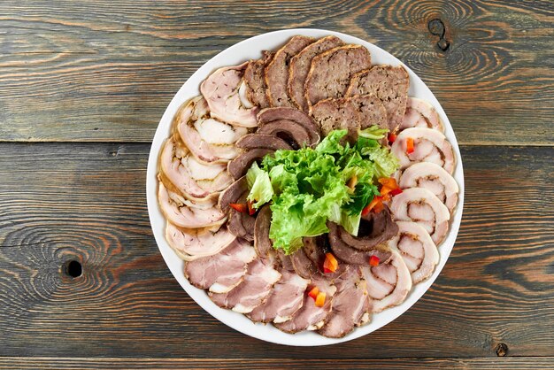 Assiette blanche sur une table en bois pleine de tranches de viande farcies, décorées de feuilles de laitue fraîche et de morceaux de paprika.