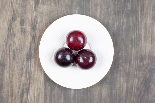 Une assiette blanche avec trois prunes fraîches sur une table en bois. Photo de haute qualité