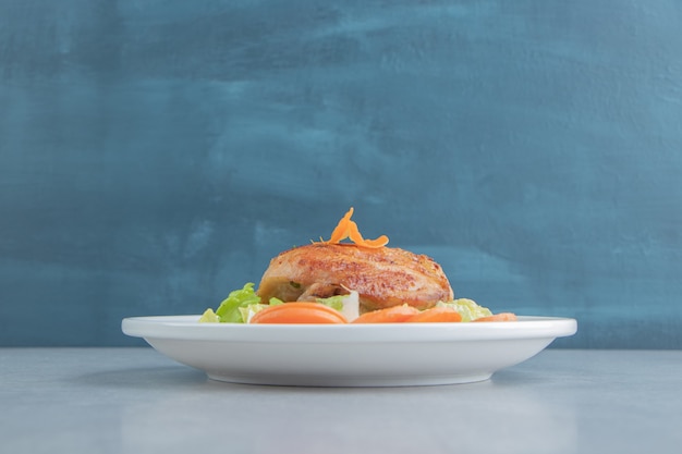 Une assiette blanche de viande frite de poulet et de carottes tranchées.