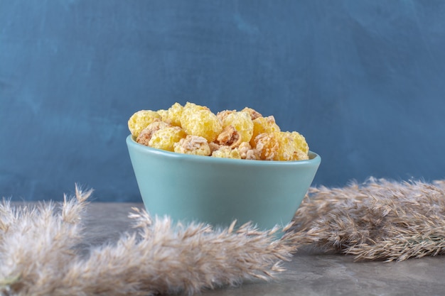 Une assiette bleue de cornflakes sucrés sains sur une table grise.