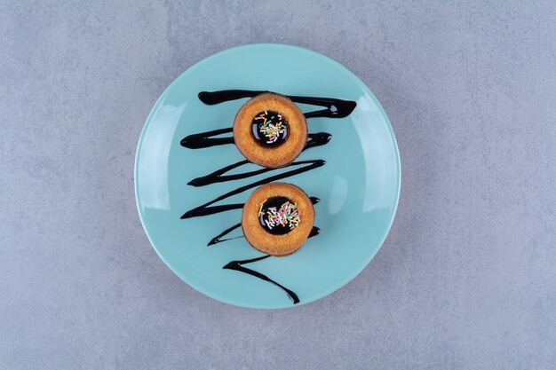 Une assiette bleue de deux beignets sucrés avec des paillettes colorées.