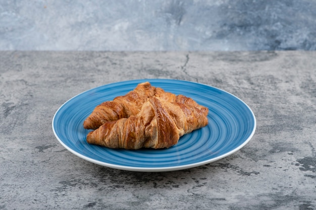 Une assiette bleue de deux croissants frais sur une table en pierre.