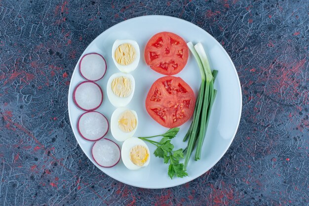 Une assiette bleue d'œufs durs avec des légumes.