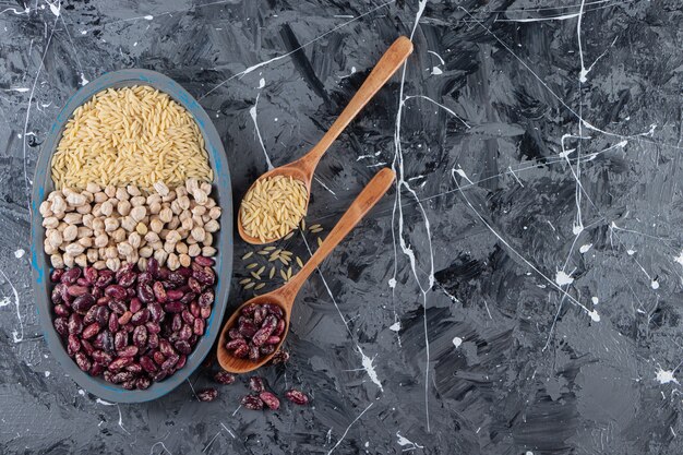 Assiette bleue pleine de pois chiches crus, de riz et de haricots sur fond de marbre.