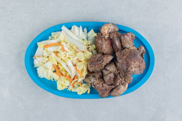 Une assiette en bois bleu de viande frite et salade de légumes.