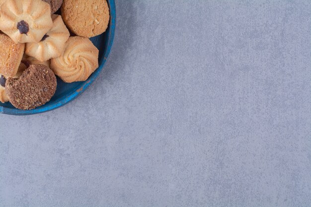 Une assiette en bois bleue avec différents biscuits sucrés.