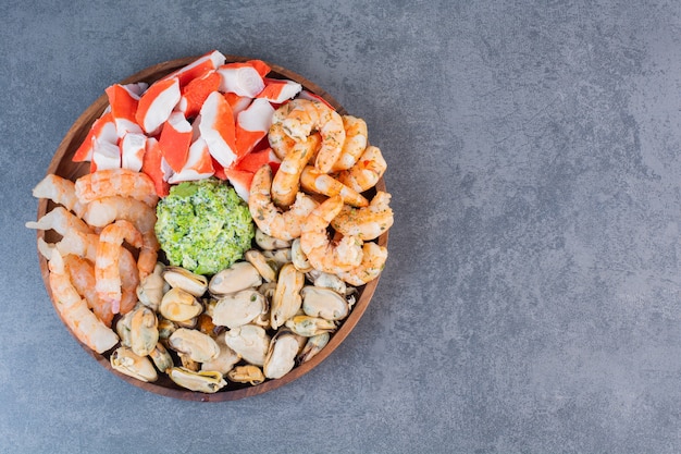 Une assiette en bois de délicieuses crevettes avec de savoureux bâtonnets de crabe sur une surface en pierre