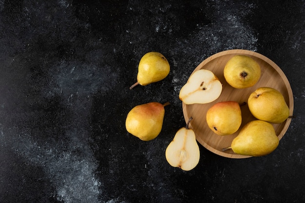 Photo gratuite assiette en bois de délicieuses poires jaunes sur une surface noire.