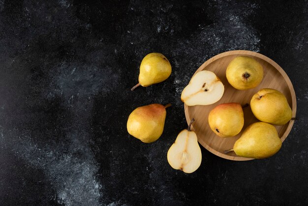 Assiette en bois de délicieuses poires jaunes sur une surface noire.