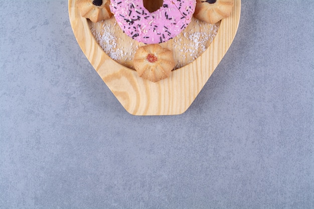 Une assiette en bois de délicieux beignet rose avec un biscuit sucré.