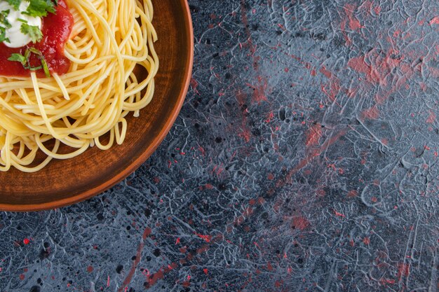 Assiette en bois de délicieux spaghettis à la sauce tomate sur une surface en marbre.