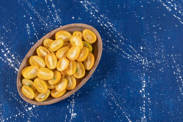 Assiette en bois de fruits kumquat tranchés sur une surface en marbre.