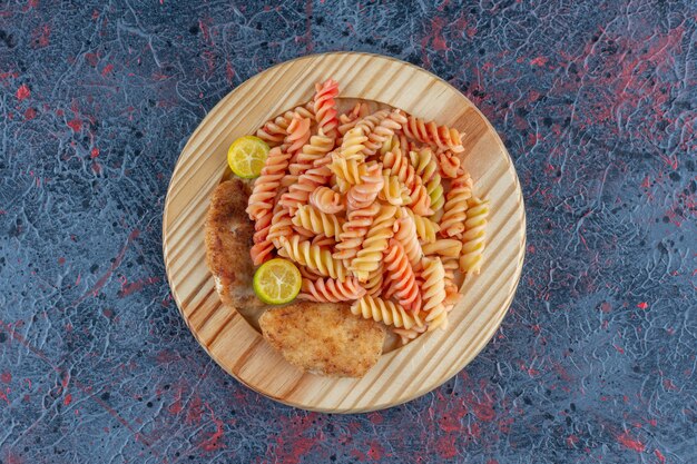 Une assiette en bois de macaronis en spirale avec de la viande de cuisse de poulet.