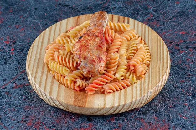 Une assiette en bois de macaronis en spirale avec de la viande de cuisse de poulet