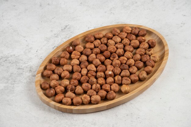 Assiette en bois de noisettes fraîches sur table en marbre.