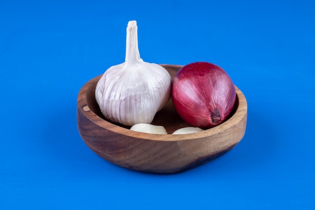 Assiette en bois d'oignon violet et d'ail sur une surface bleue