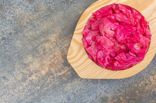 Une assiette en bois pleine de chou salé rouge sur fond de marbre. photo de haute qualité