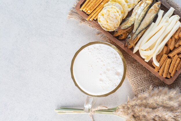 Une assiette en bois pleine de délicieux poissons et fromages avec de la bière et des petits pois.