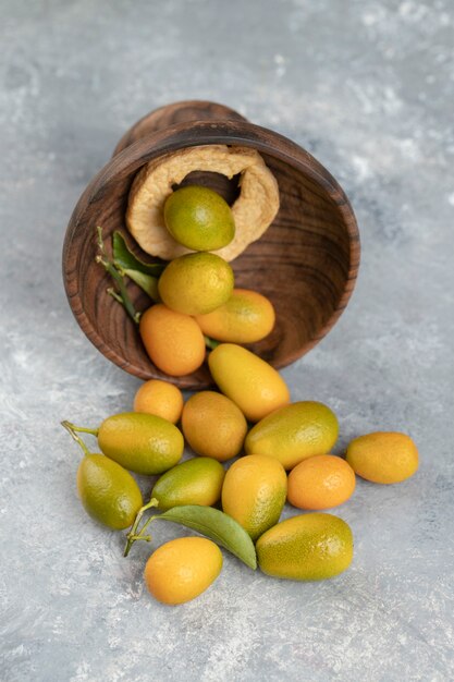 Une assiette en bois pleine de kumquats frais jaunes avec des feuilles sur un marbre.