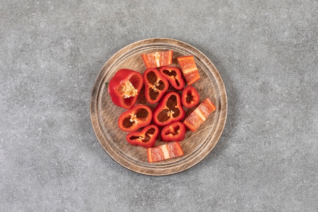 Assiette en bois de poivrons rouges frais tranchés sur une surface en marbre.