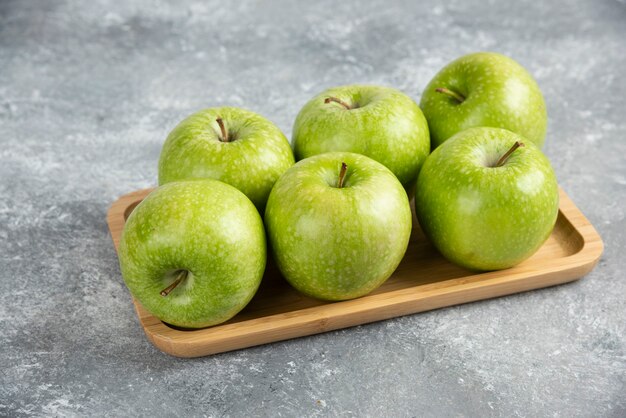 Assiette en bois de pommes vertes brillantes sur table en marbre.