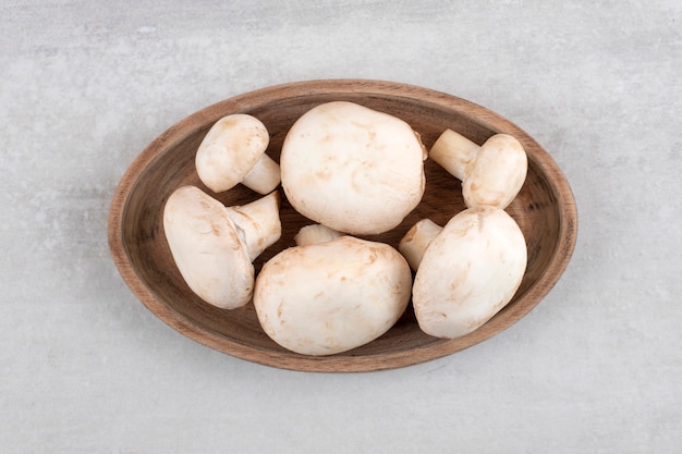 Une assiette en bois remplie de champignons frais placés sur une surface en pierre