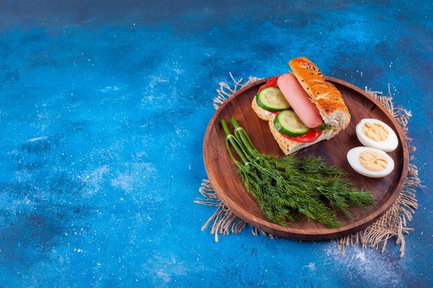 Assiette en bois de sandwich à la saucisse à l'aneth et oeufs sur une surface bleue.