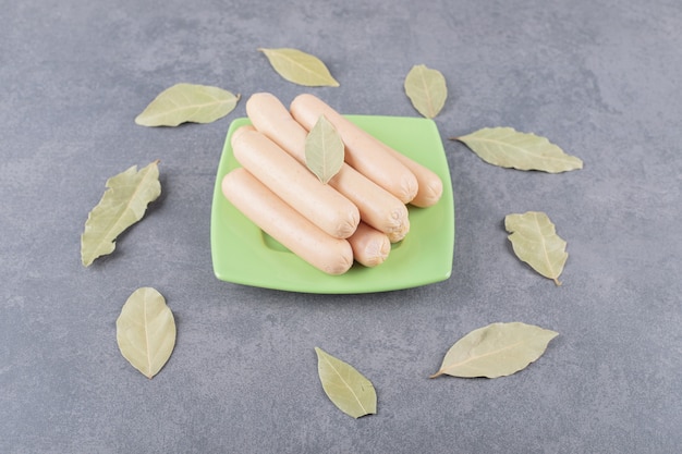 Photo gratuite une assiette en bois avec des saucisses bouillies et des feuilles de laurier