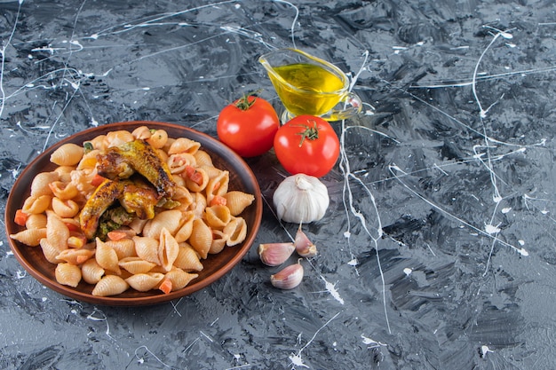 Assiette en bois de savoureuses pâtes aux coquillages avec aile de poulet sur une surface en marbre.