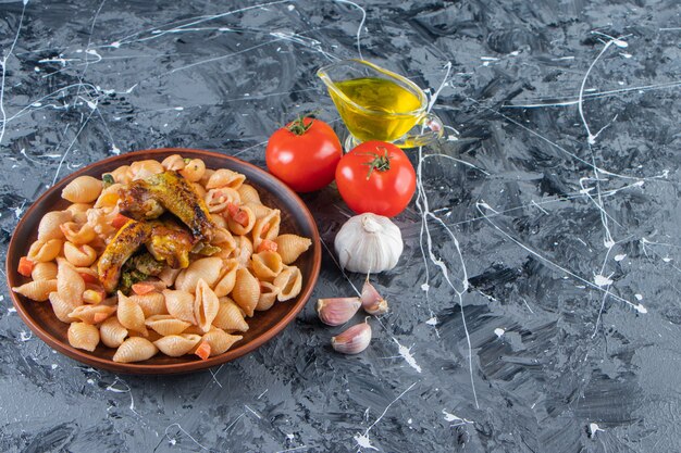 Assiette en bois de savoureuses pâtes aux coquillages avec aile de poulet sur une surface en marbre.