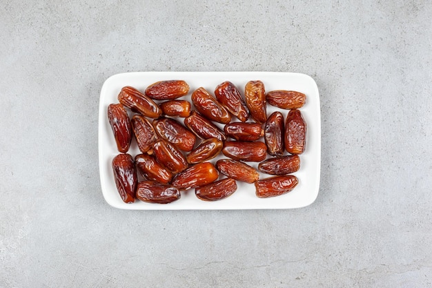 Photo gratuite assiette carrée pleine de dattes sur une surface en marbre