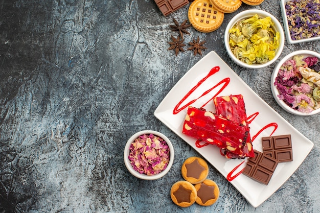 Une assiette de chocolat avec des biscuits et des fleurs sèches autour d'elle sur fond gris