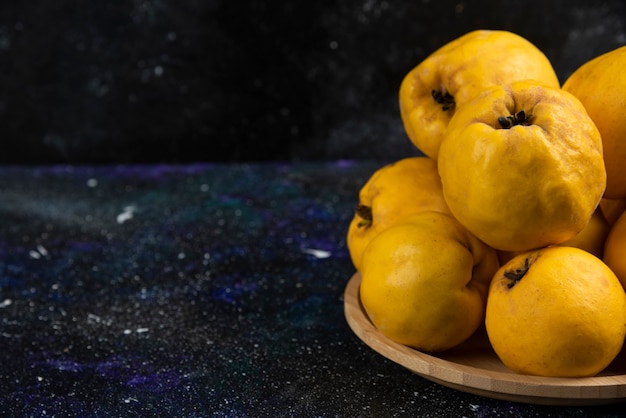 Assiette de coings frais placés sur une table sombre.