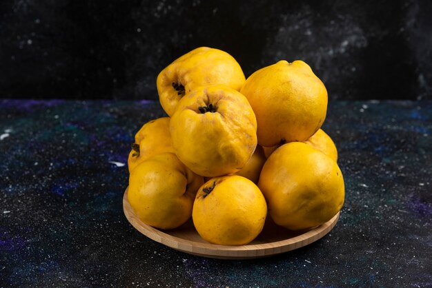 Assiette de coings frais placés sur une table sombre.