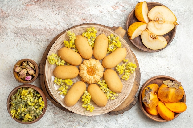 Une assiette de cookies sur un plateau en bois et des fruits et des fleurs sèches autour d'elle sur un sol en marbre