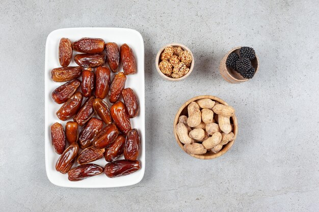 Assiette de dattes à côté de bols d'arachides et de mûres sur une surface en marbre. Illustration de haute qualité