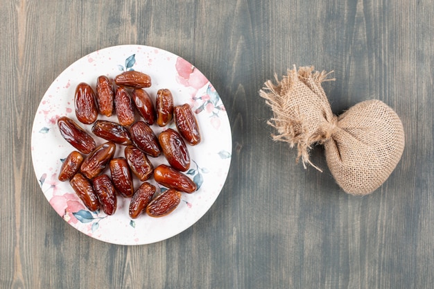 Photo gratuite assiette de dattes sur une surface en bois avec un sac