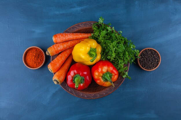 Assiette de divers légumes frais et mûrs sur une surface bleue.