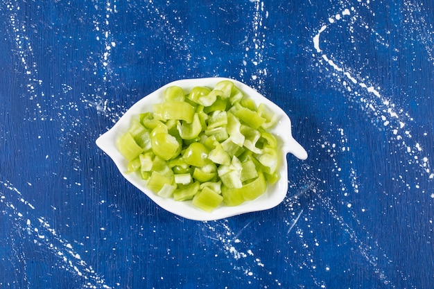 Assiette en forme de feuille de poivrons verts tranchés sur une surface en marbre.