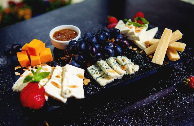 Assiette de fromage avec des cubes de cheddar, du fromage blanc, des bâtonnets de parmesan, du fromage bleu et des raisins