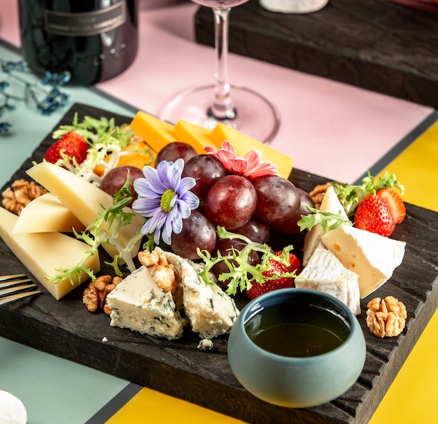 Photo gratuite assiette de fromages avec cheddar, chèvre, gouda, fromage bleu, miel, raisin et fleurs