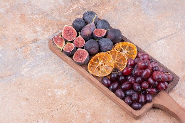 Assiette de fruits en bois avec figues, baies de coin et tranches d'orange sèches.