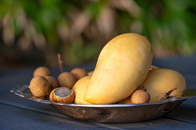 Une assiette de fruits tropicaux sur une table en bois. Mangue jaune et litchi sur fond flou.