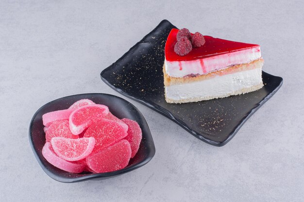 Assiette de gâteau au fromage et bol de bonbons sur une surface en marbre.