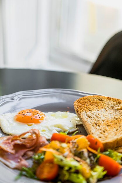 Assiette grise avec oeuf pour le petit-déjeuner; Bacon; pain grillé et salade sur la table